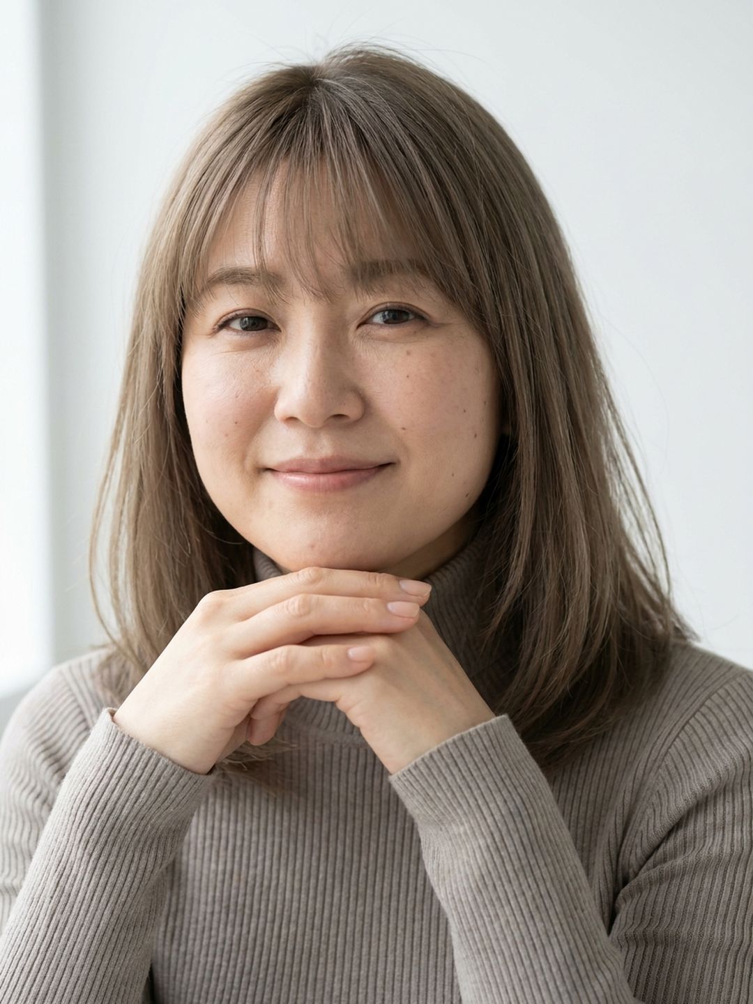 あごの下で手を重ねて微笑む40代の女性（イメージ）