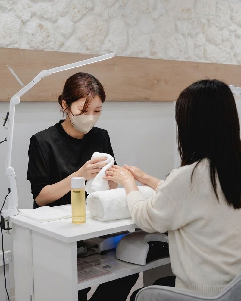 ハンドバスで温まった手を、ネイリストがタオルで包んでいる