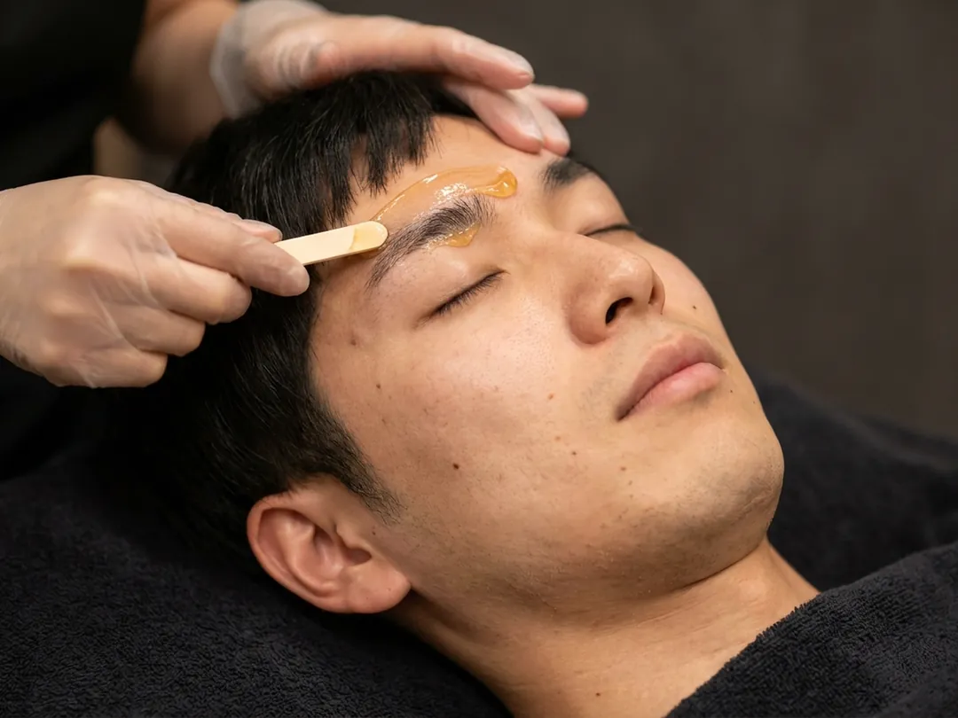 目を閉じた男性の眉にワックスをのせる施術イメージ