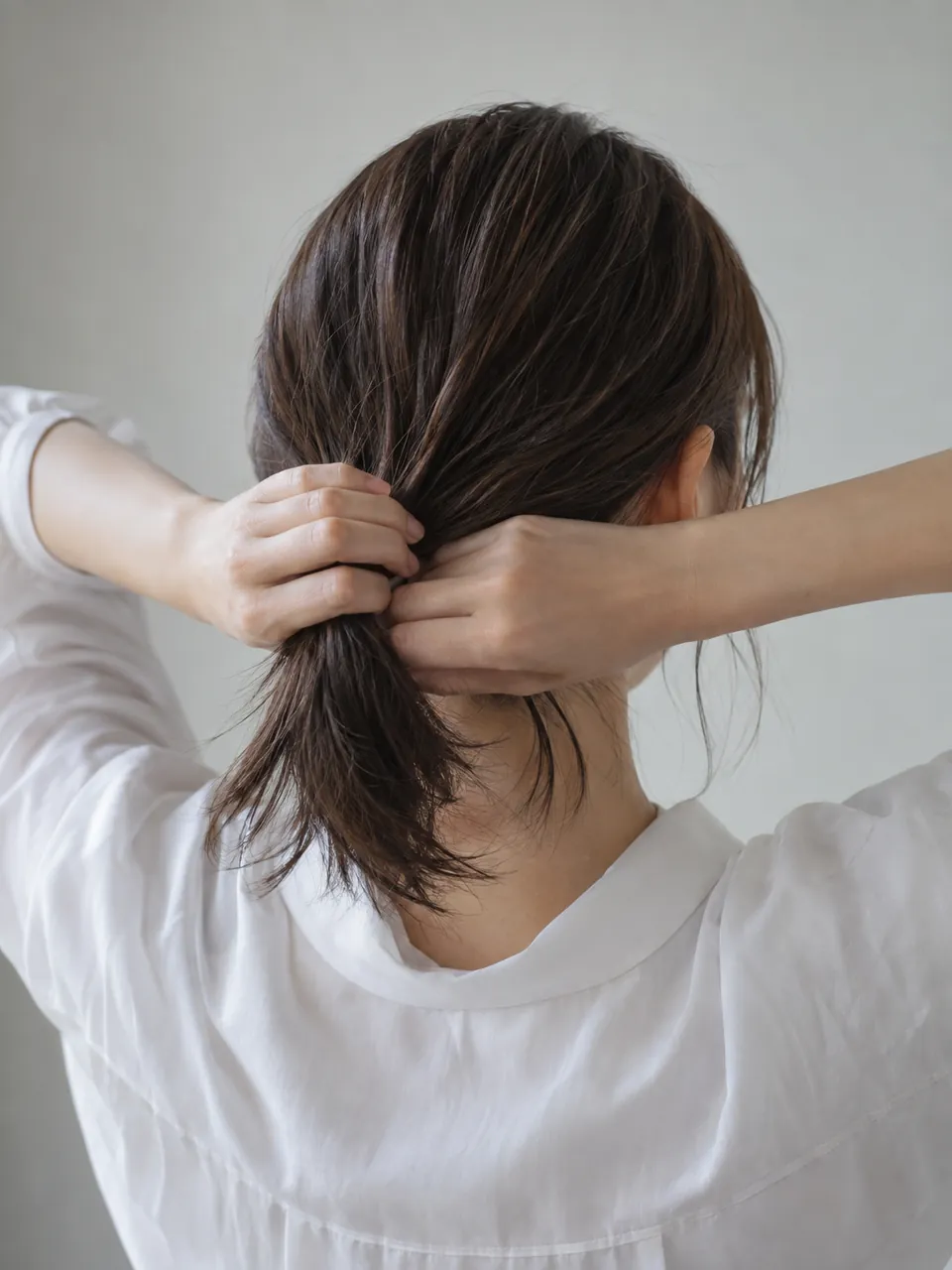 伸びた段の髪を襟足で結ぼうとする女性の後ろ姿のイメージ